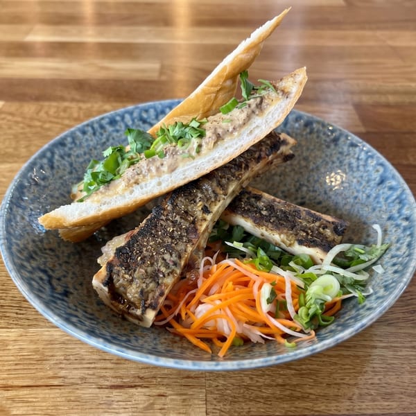 Grilled bone marrow with a baguette, topped with a creamy spread, cilantro, and pickled vegetables.