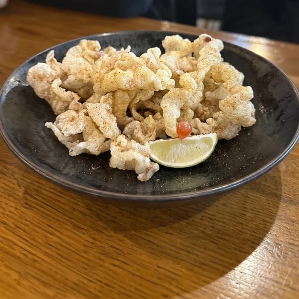Crispy chicharrones seasoned with spices, garnished with a lime wedge and a small red berry.