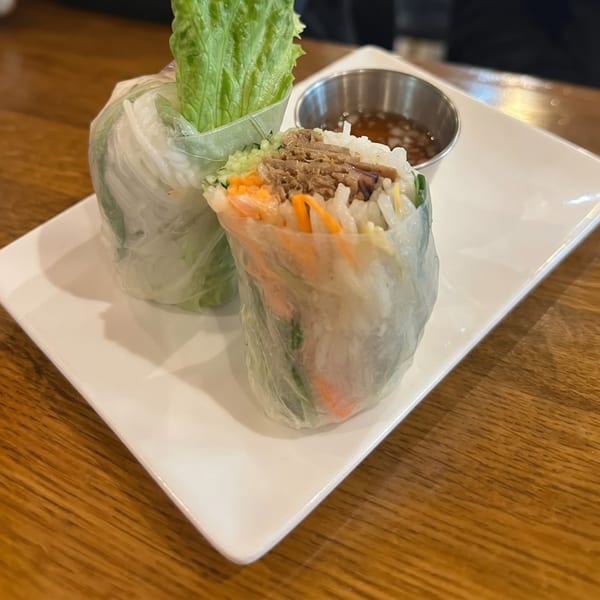 Two fresh spring rolls with lettuce, meat, and vegetables, served with a dipping sauce.