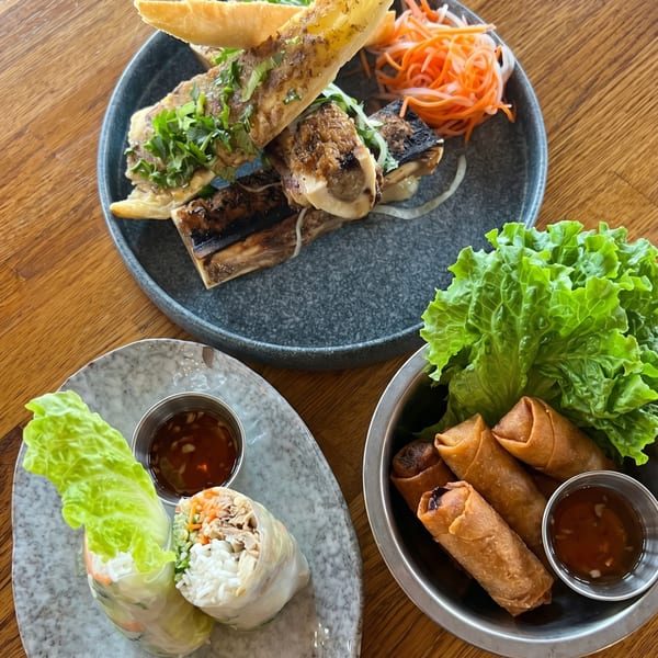 Three plates of Vietnamese food: grilled fish, spring rolls with lettuce, and fresh rolls with dipping sauce.